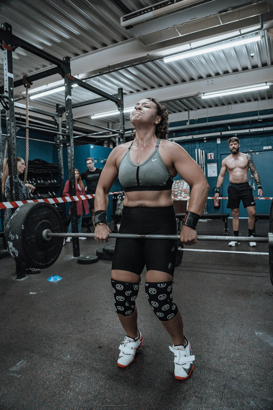 a woman standing in a gym holding a barbell