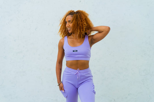 a woman with curly hair wearing a purple sports bra top and matching leggings